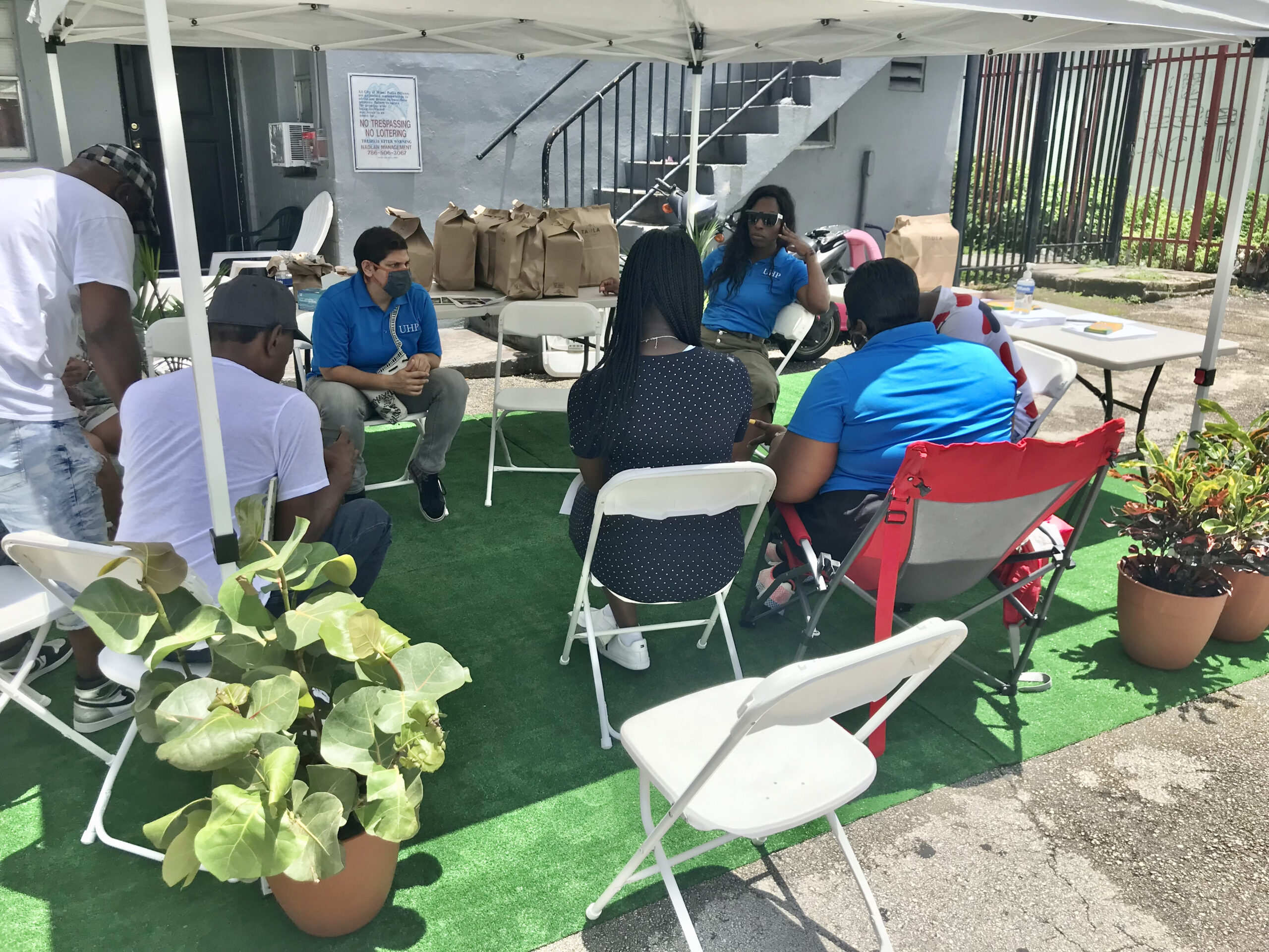 A group of people sitting around in chairs under an umbrella.