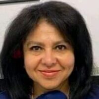 A woman with black hair and blue shirt smiling.