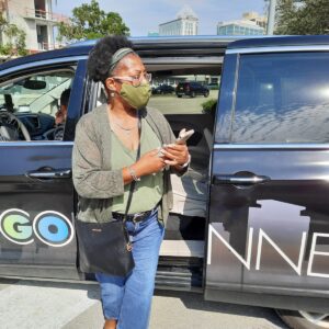 A woman in a green shirt and black jacket standing next to a car.