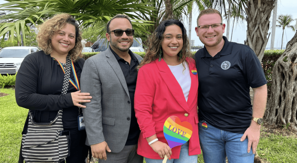 Four people smiling with rainbow love sign.